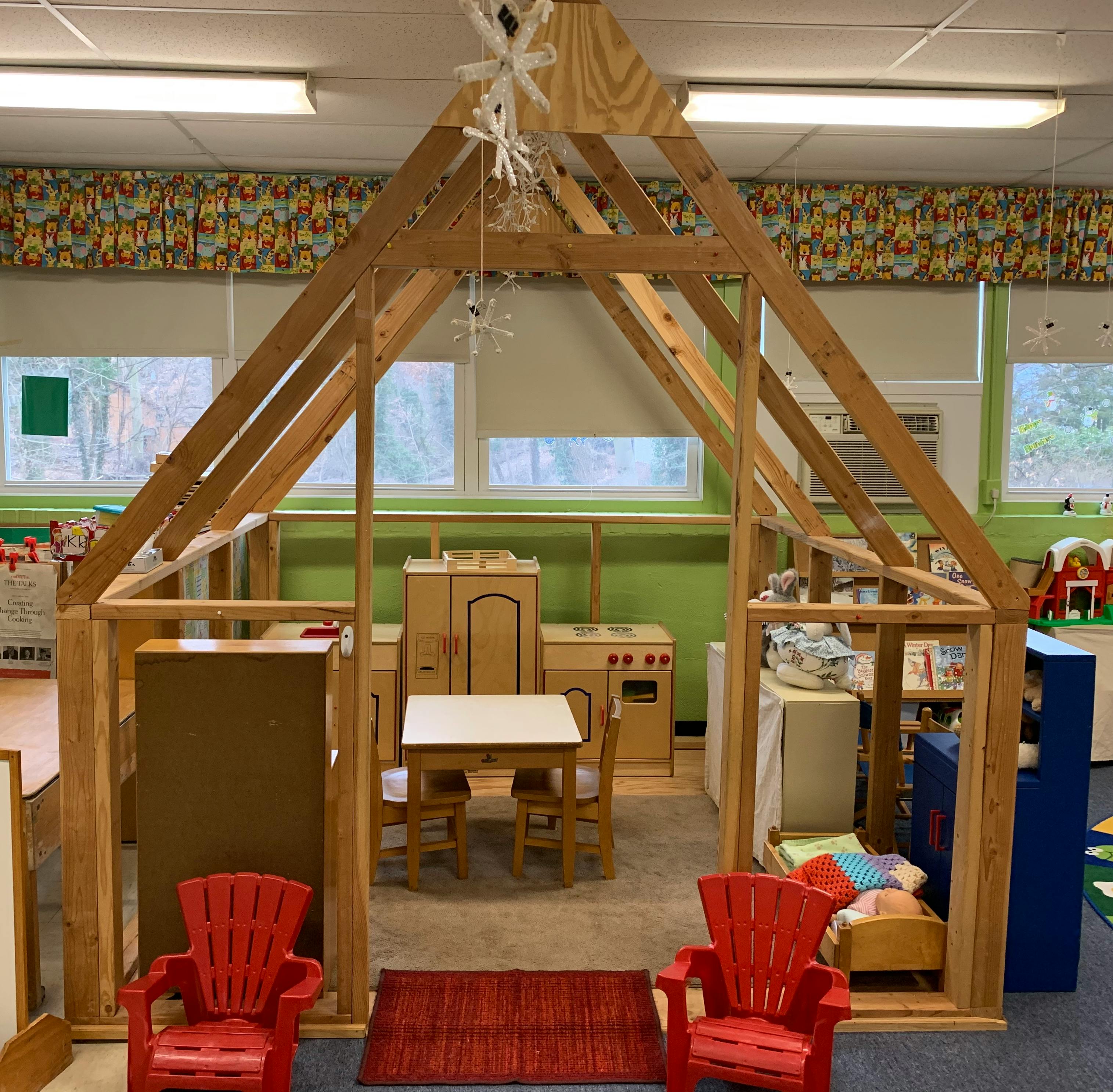 Wooden playhouse frame with miniature furniture inside a classroom
