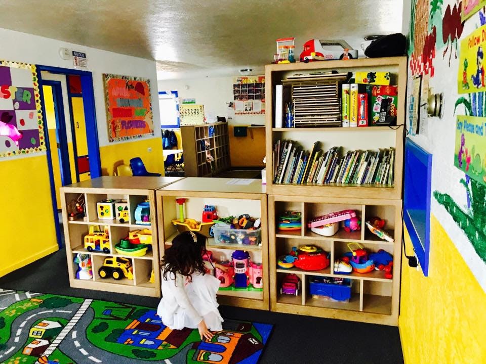 Child playing on a rug in a classroom with shelves of toys and books