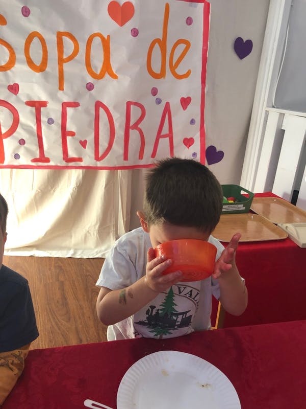 Child drinking from an orange bowl with a Sopa de Piedra sign in background