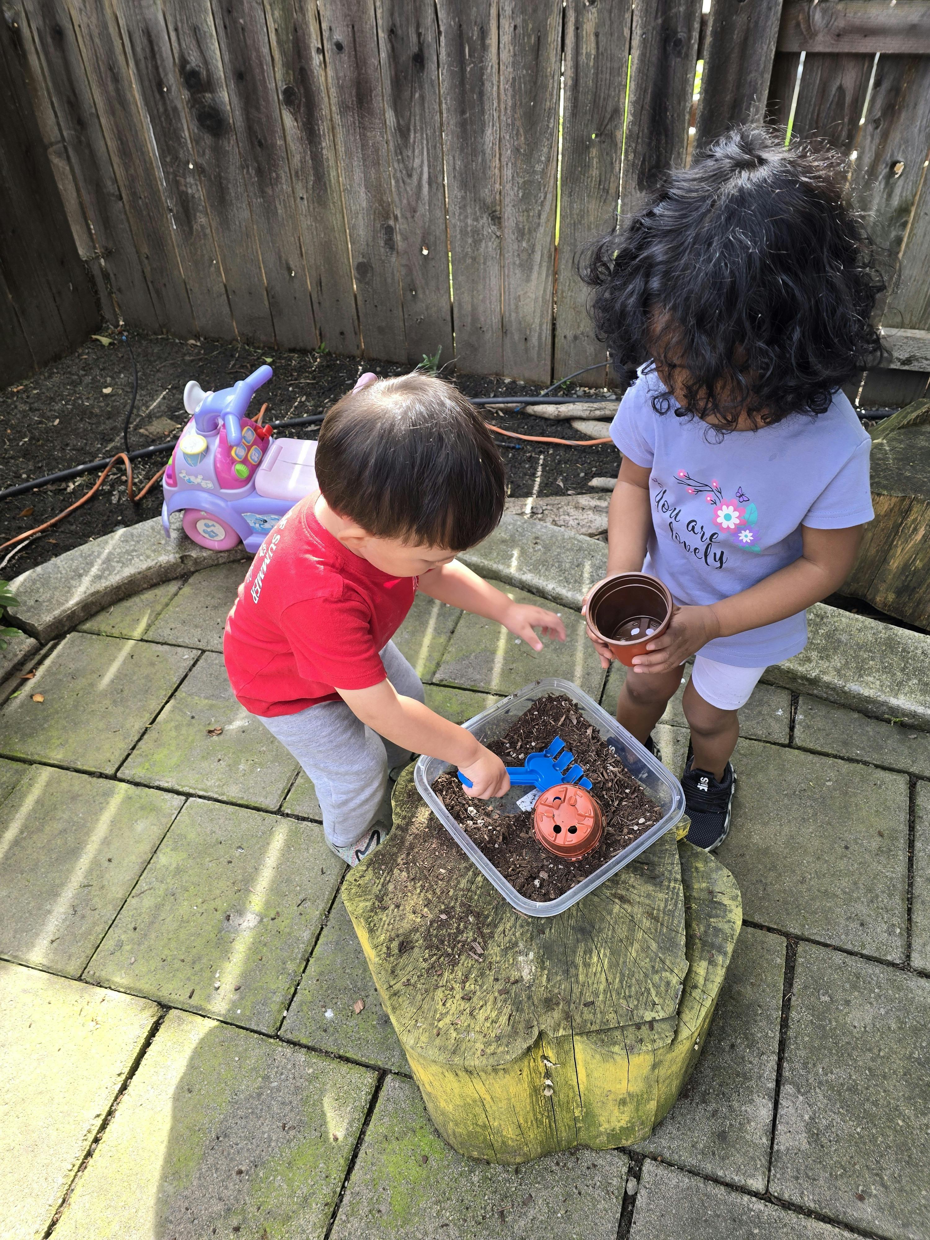 two children playing with dirt in a container, one holding a pot