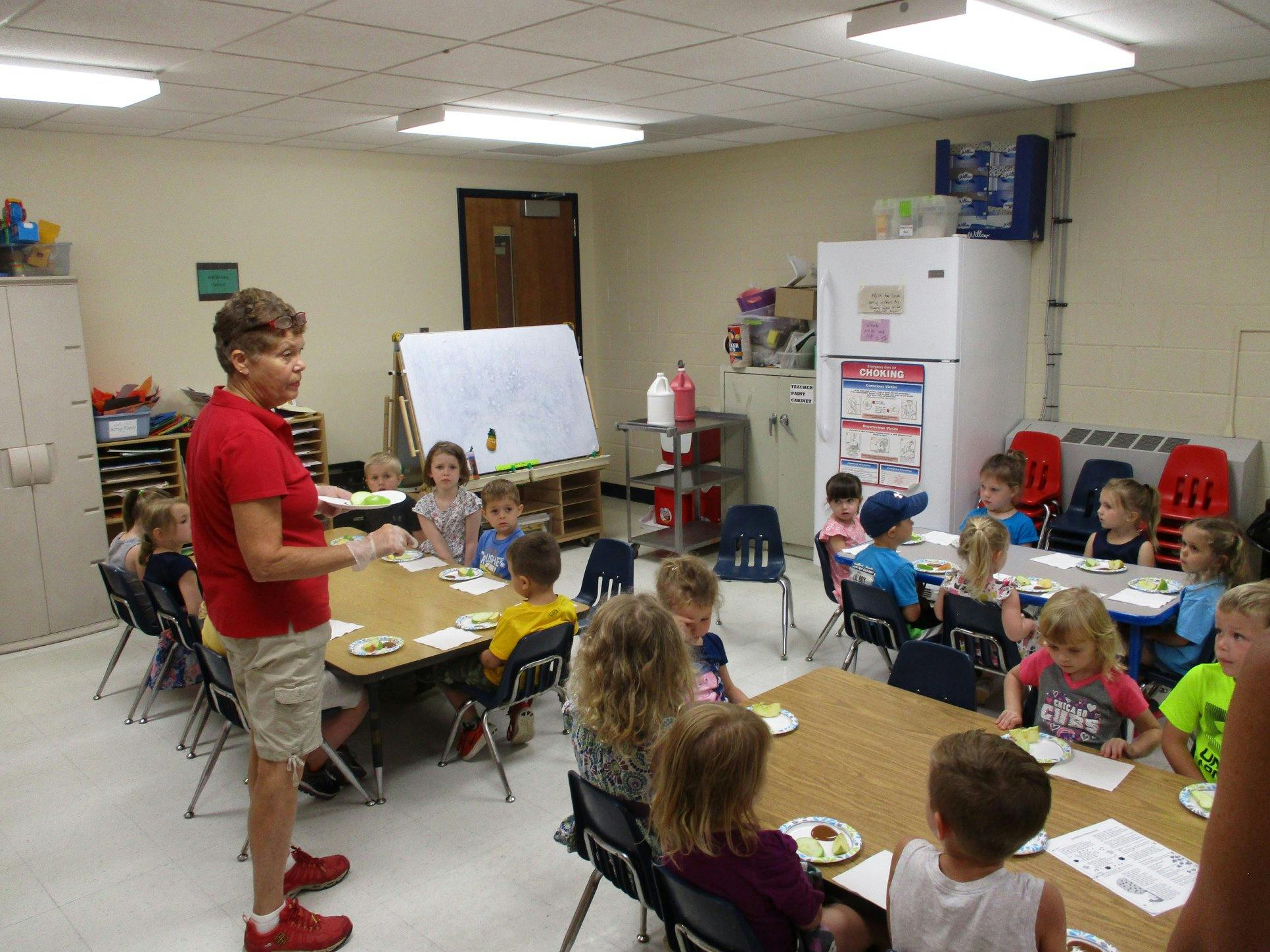 Person standing in a classroom with children seated at tables