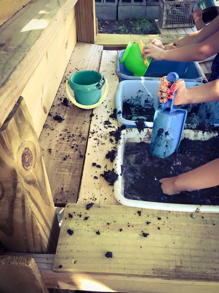 Children playing with mud and water in plastic bins