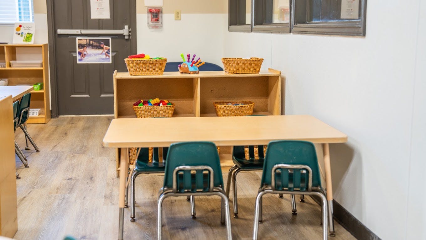 Small table and chairs with wooden shelving containing toy baskets