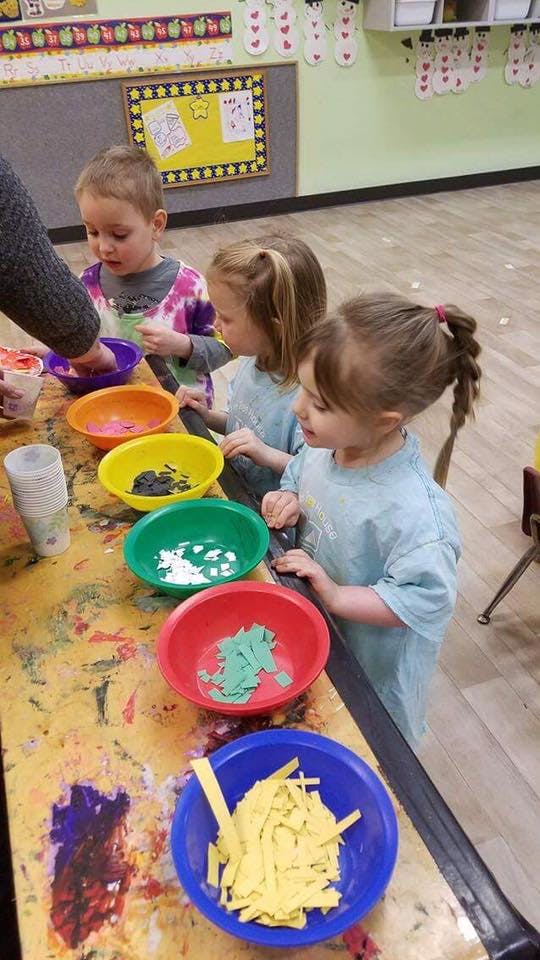 Children at a table with colorful bowls of craft supplies