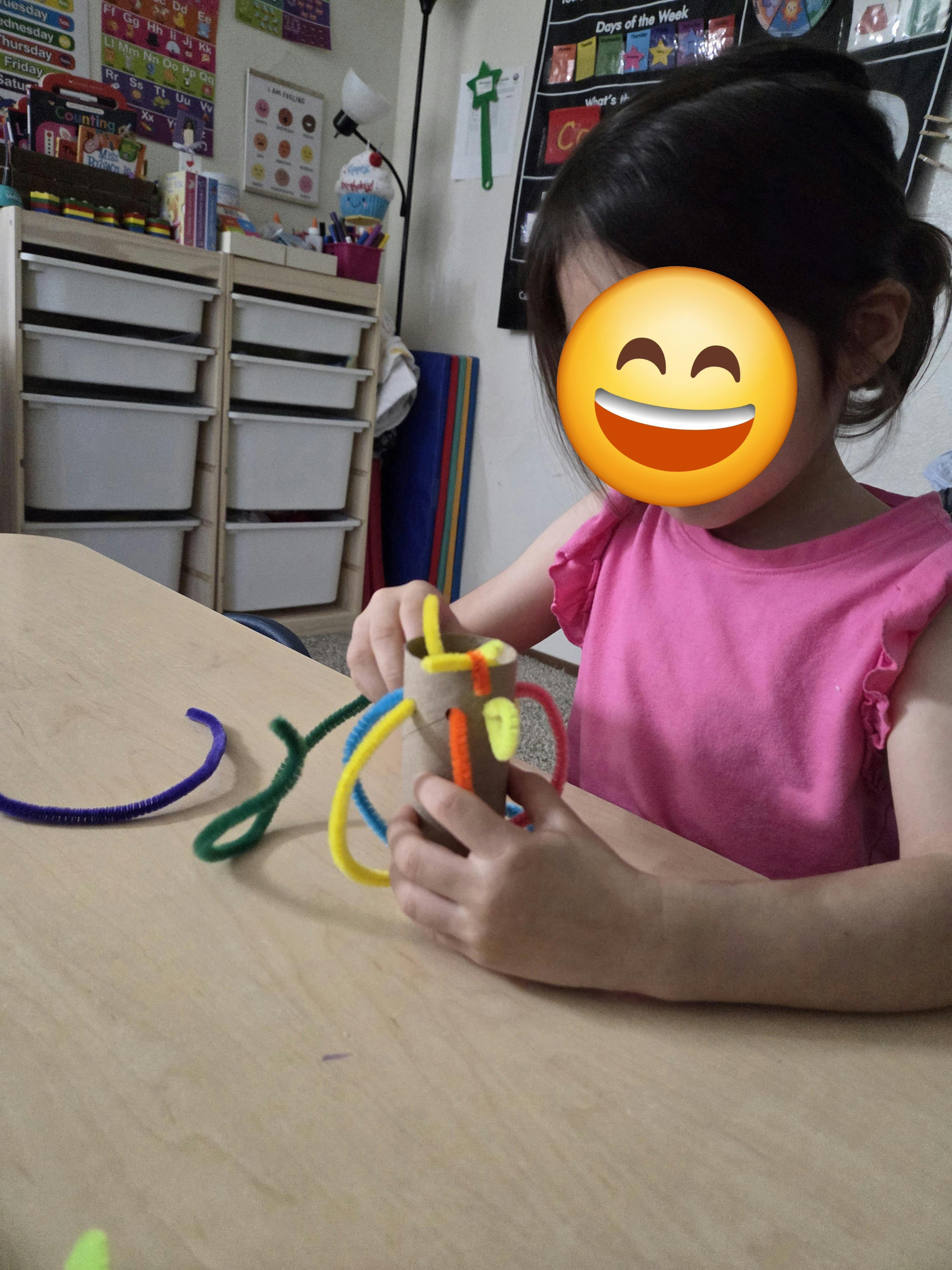 Child crafting with a cardboard tube and colorful pipe cleaners on a table