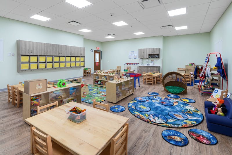 Empty colorful preschool classroom with small tables, chairs, and play areas