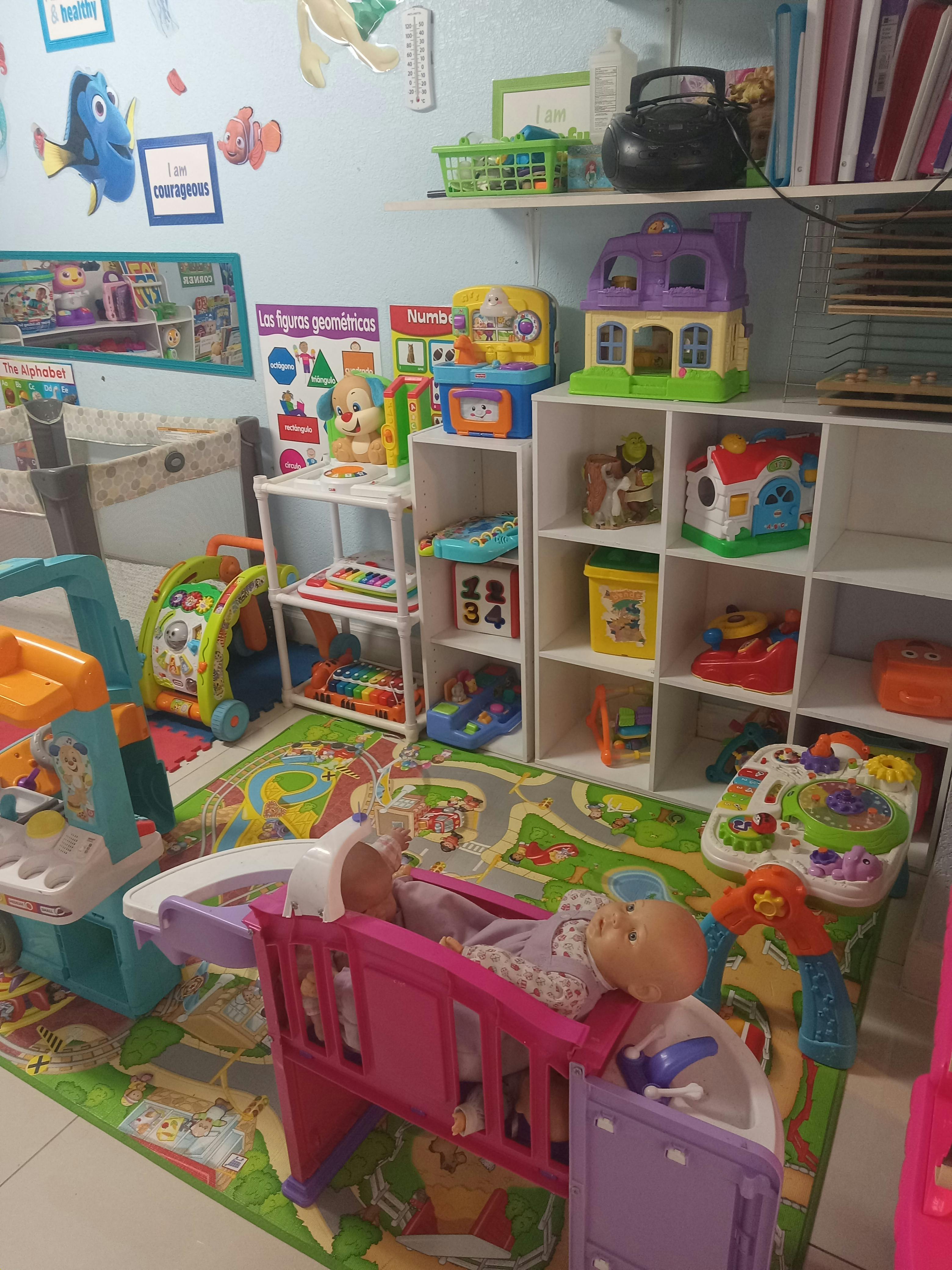 Doll in a play stroller surrounded by various learning toys and play mats