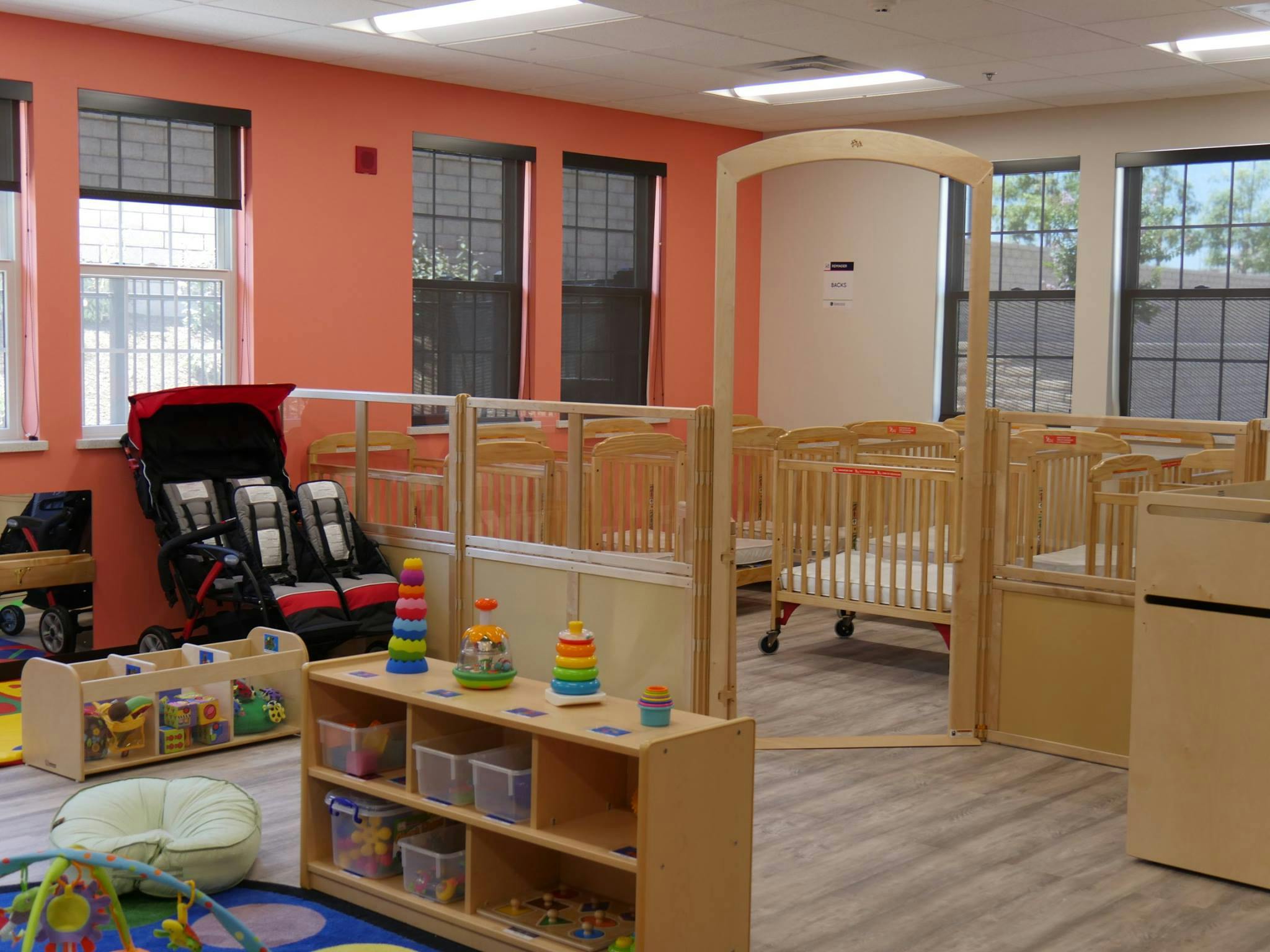 Empty nursery room with cribs, play shelves, and a stroller