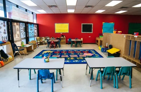Empty classroom with small tables and chairs, and a colorful rug