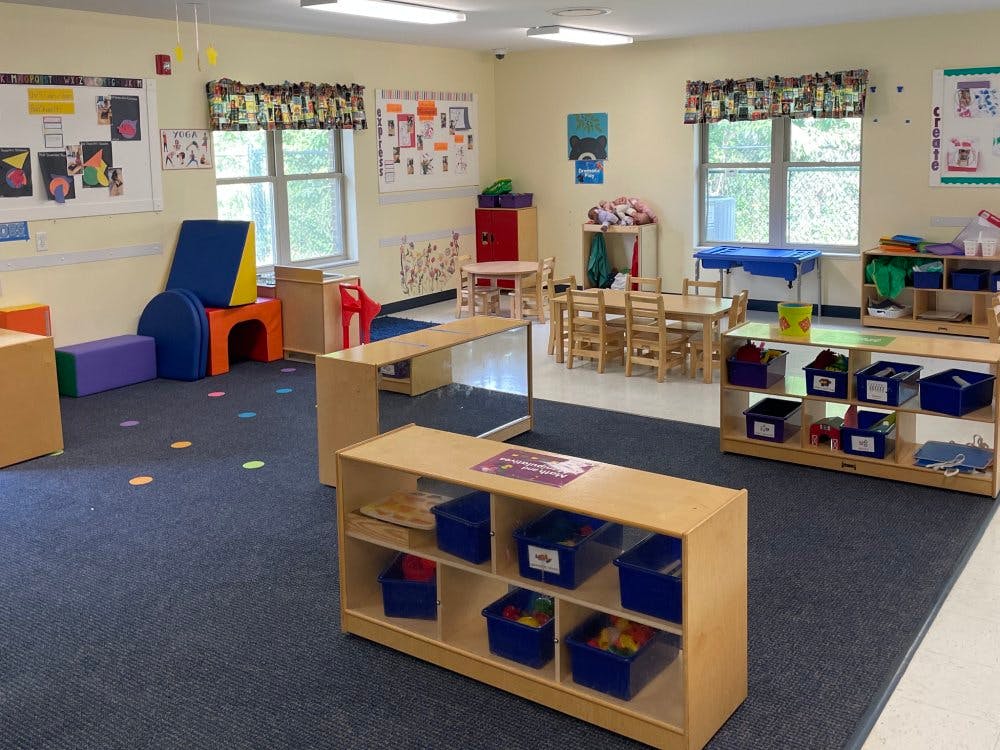 An empty classroom with small tables, chairs, and play equipment