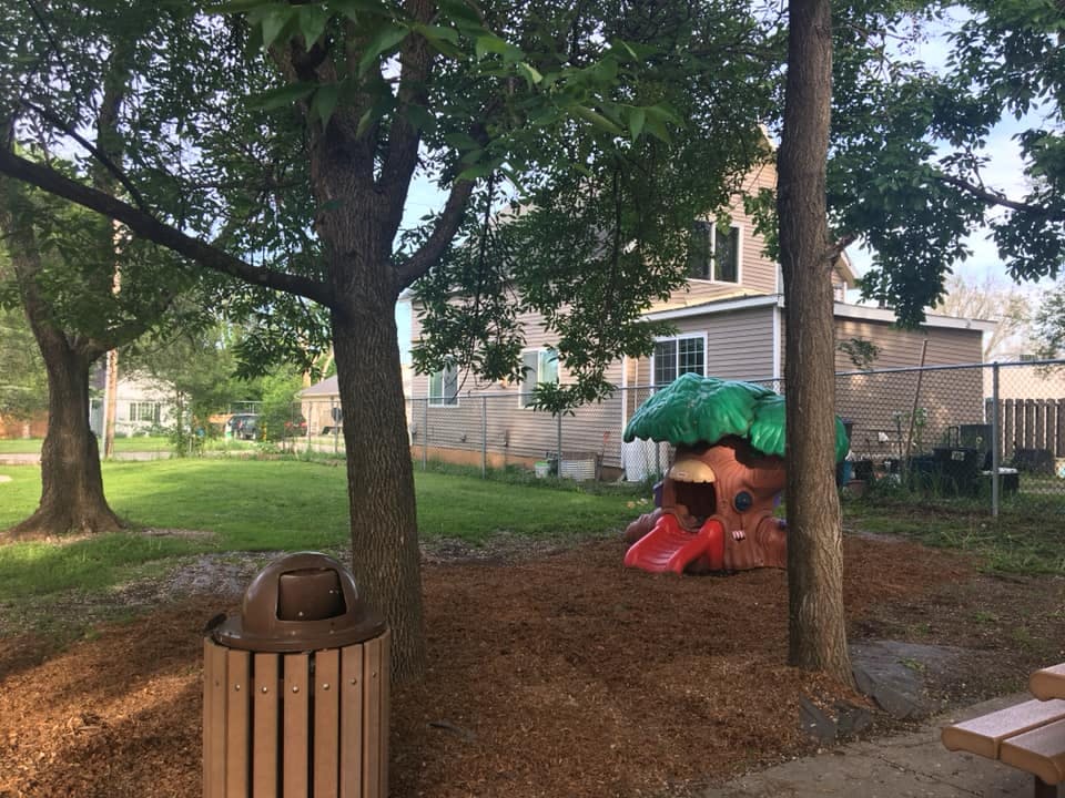 Playground with a tree-shaped slide and a trash can under a tree