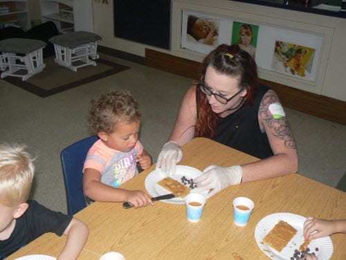 Adult in gloves helping a child with food at a table