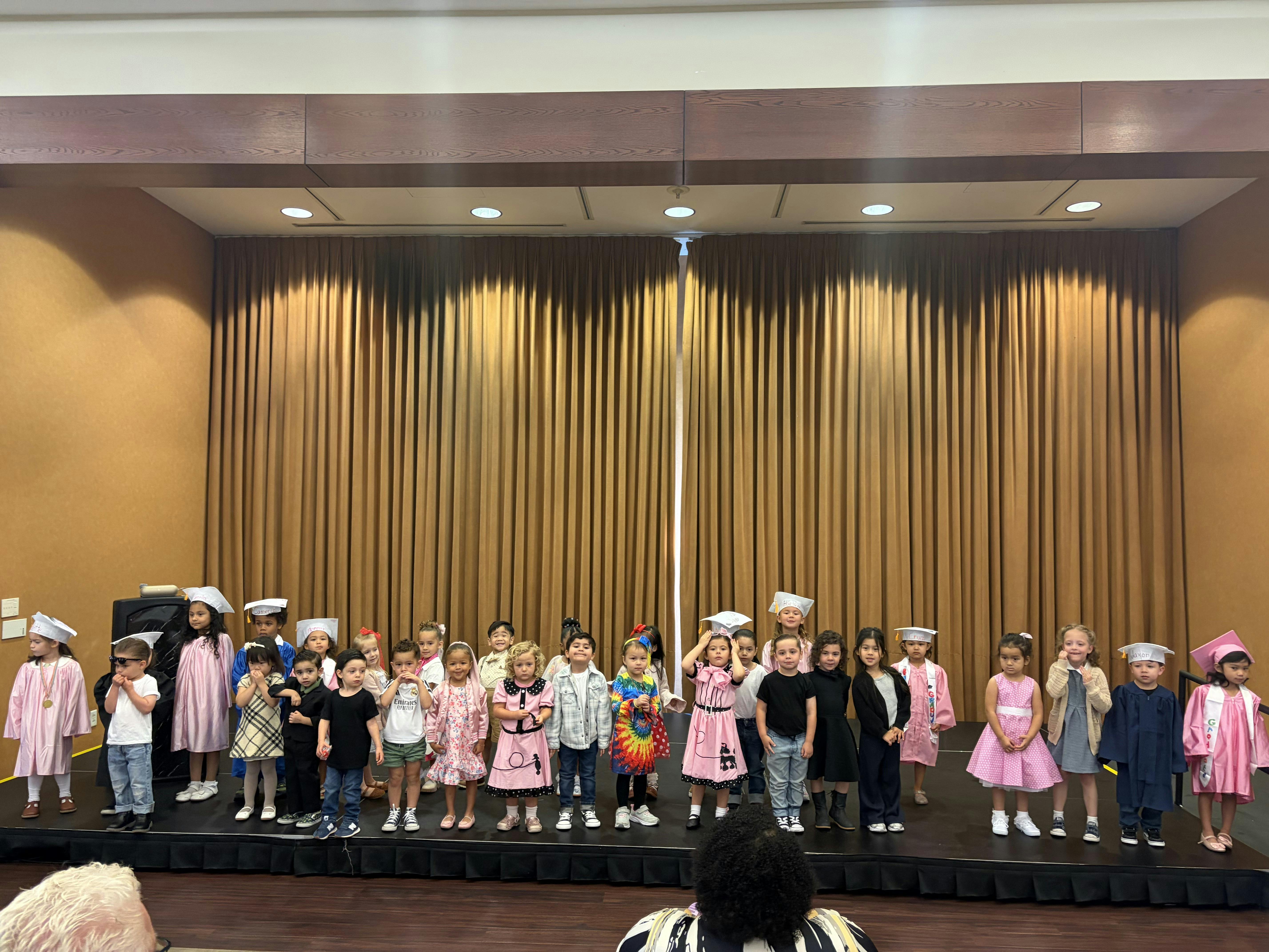 Group of children standing on a stage in front of curtains