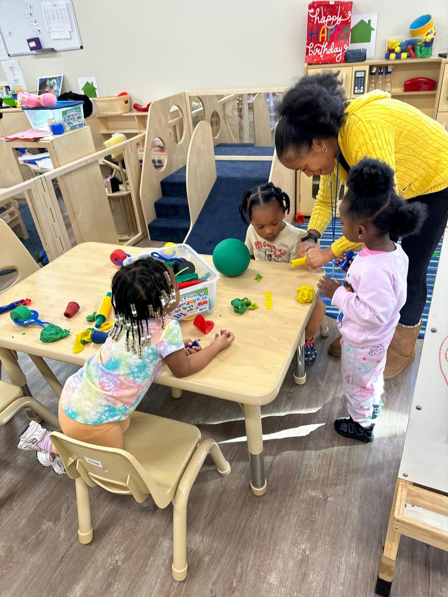 Adult and three children playing with toys at a table in a classroom