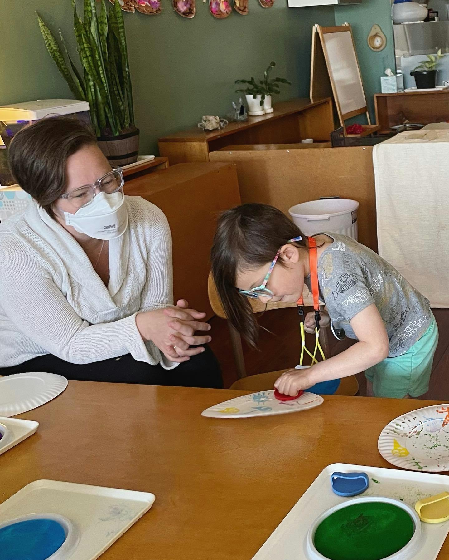 Person in mask watching child use a stamp on a paper plate