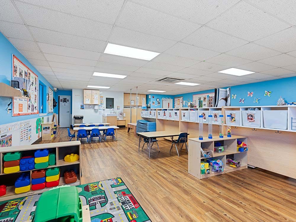 Empty classroom with light blue walls, small tables, chairs, and play items