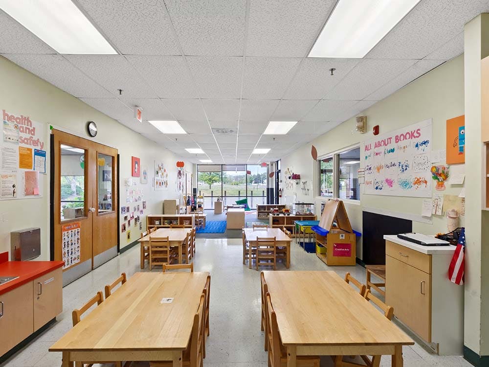 Empty classroom with small wooden tables and chairs, artwork on walls