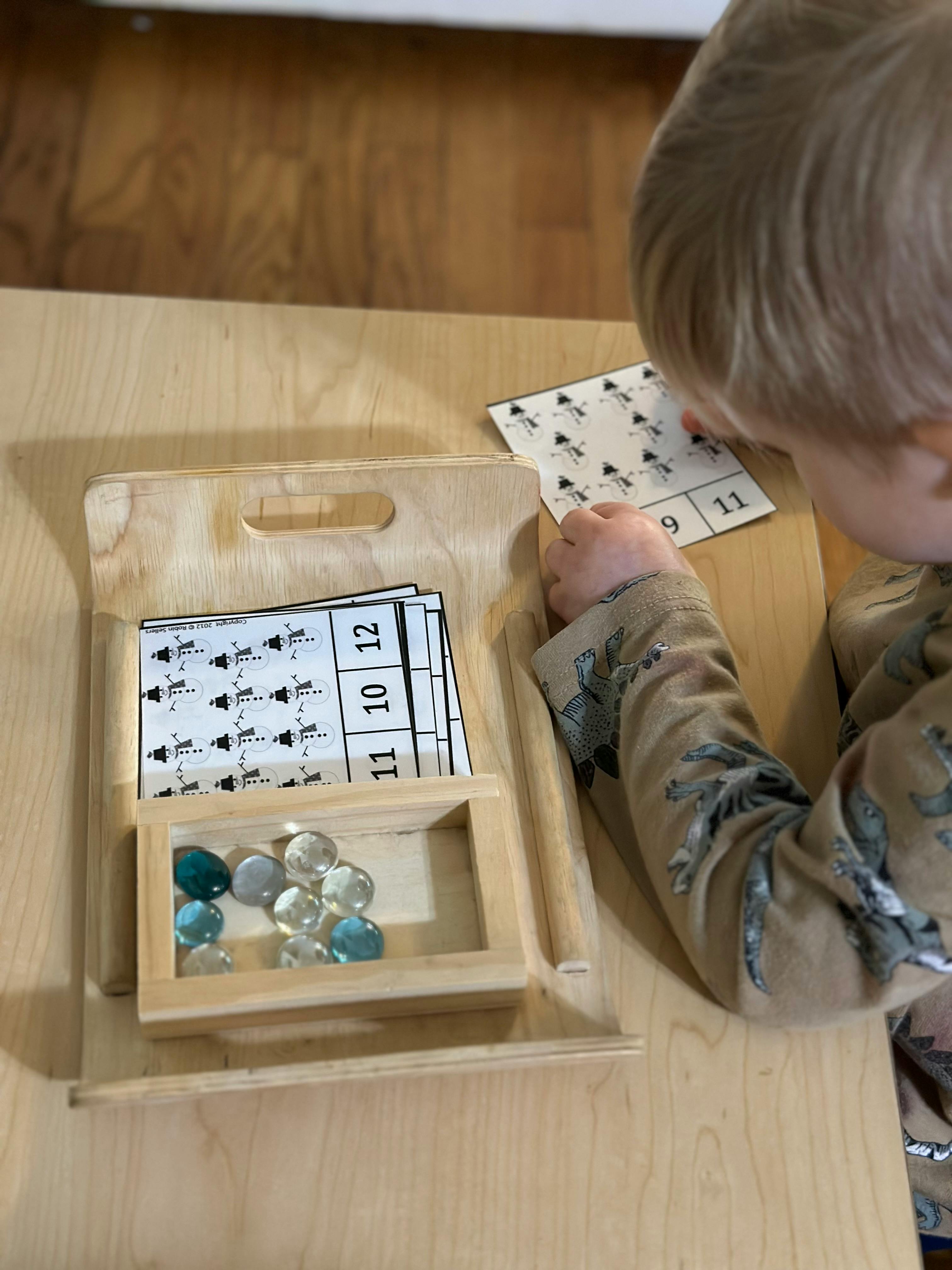 Child holding a number card with a wooden tray of cards and glass beads