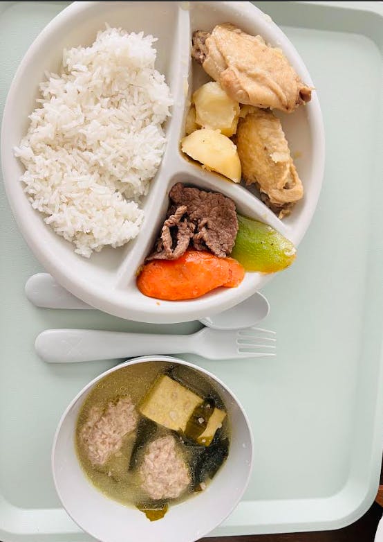 A divided plate of rice, chicken wings, potatoes, beef, and vegetables with a side of soup