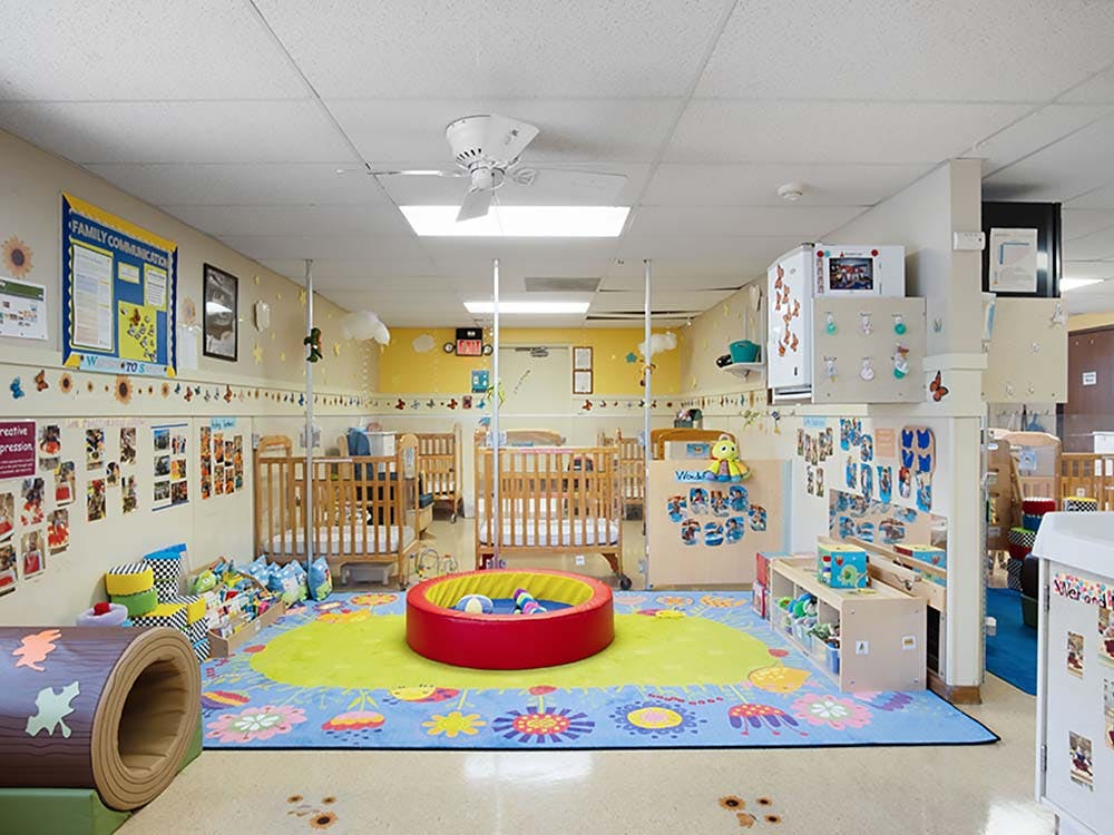 A colorful childcare room with cribs, play mats, and toys