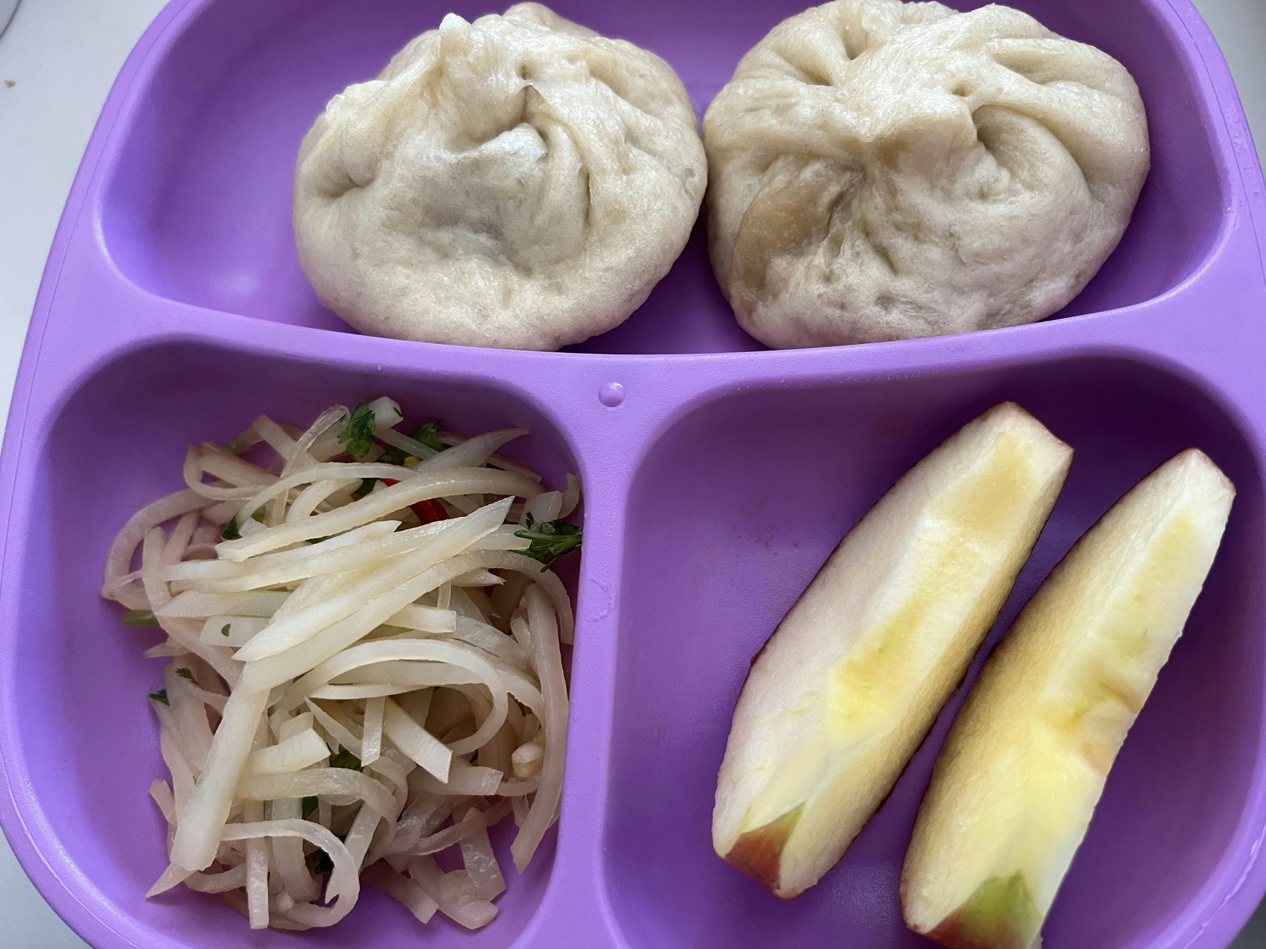 Steamed buns, shredded daikon salad, and apple slices in a divided purple plate