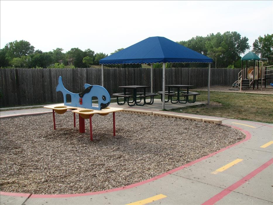 Playground with a whale-shaped sand and water table, picnic tables under a blue canopy