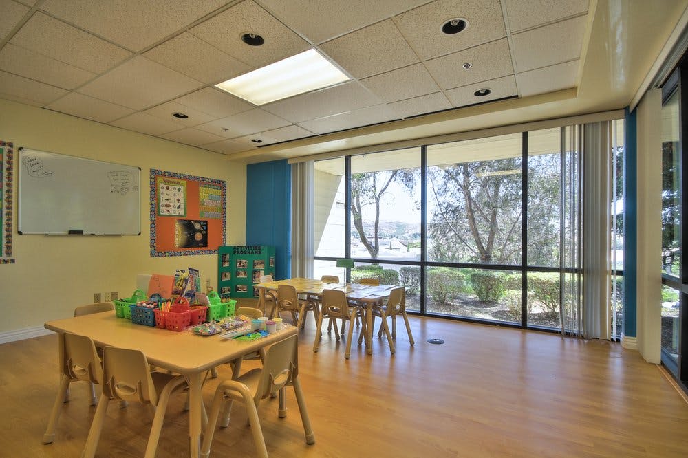 Classroom with small tables and chairs, large windows overlooking trees
