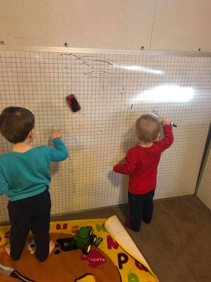Two children drawing on a grid whiteboard