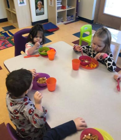 Three children eating at a table in a classroom