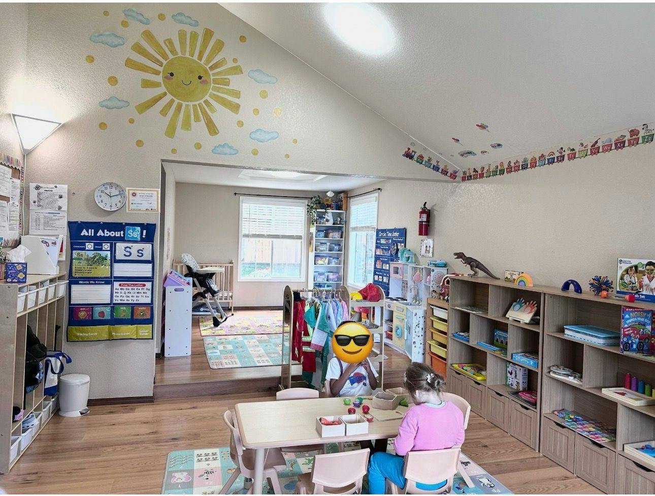 Two children sitting at a table in a playroom with educational wall decor