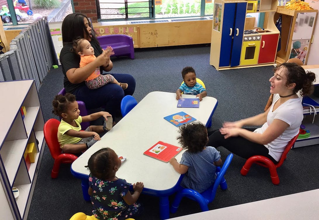 Two adults and multiple children sitting around a table in a classroom