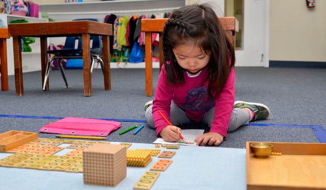 Child drawing on paper on the floor with math manipulatives