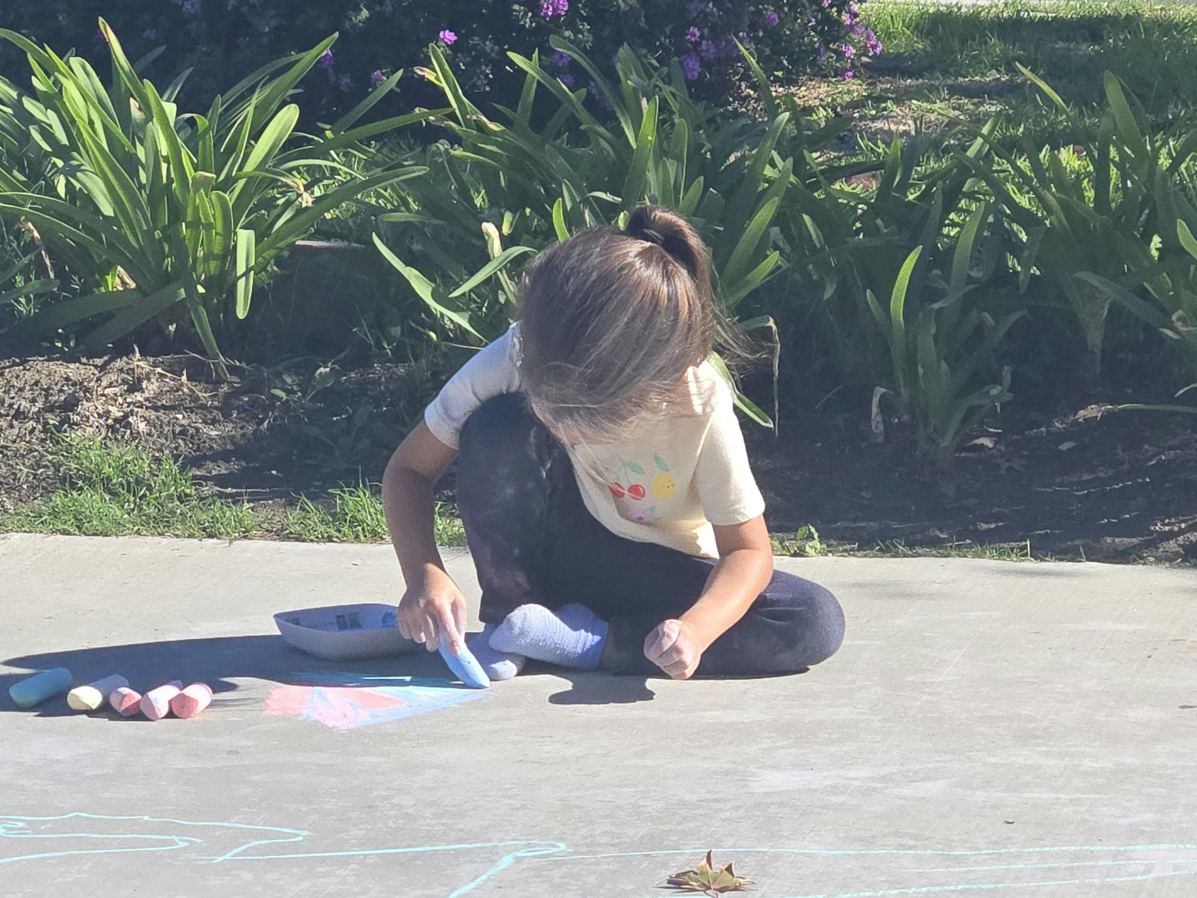 Child sitting on the ground drawing with chalk