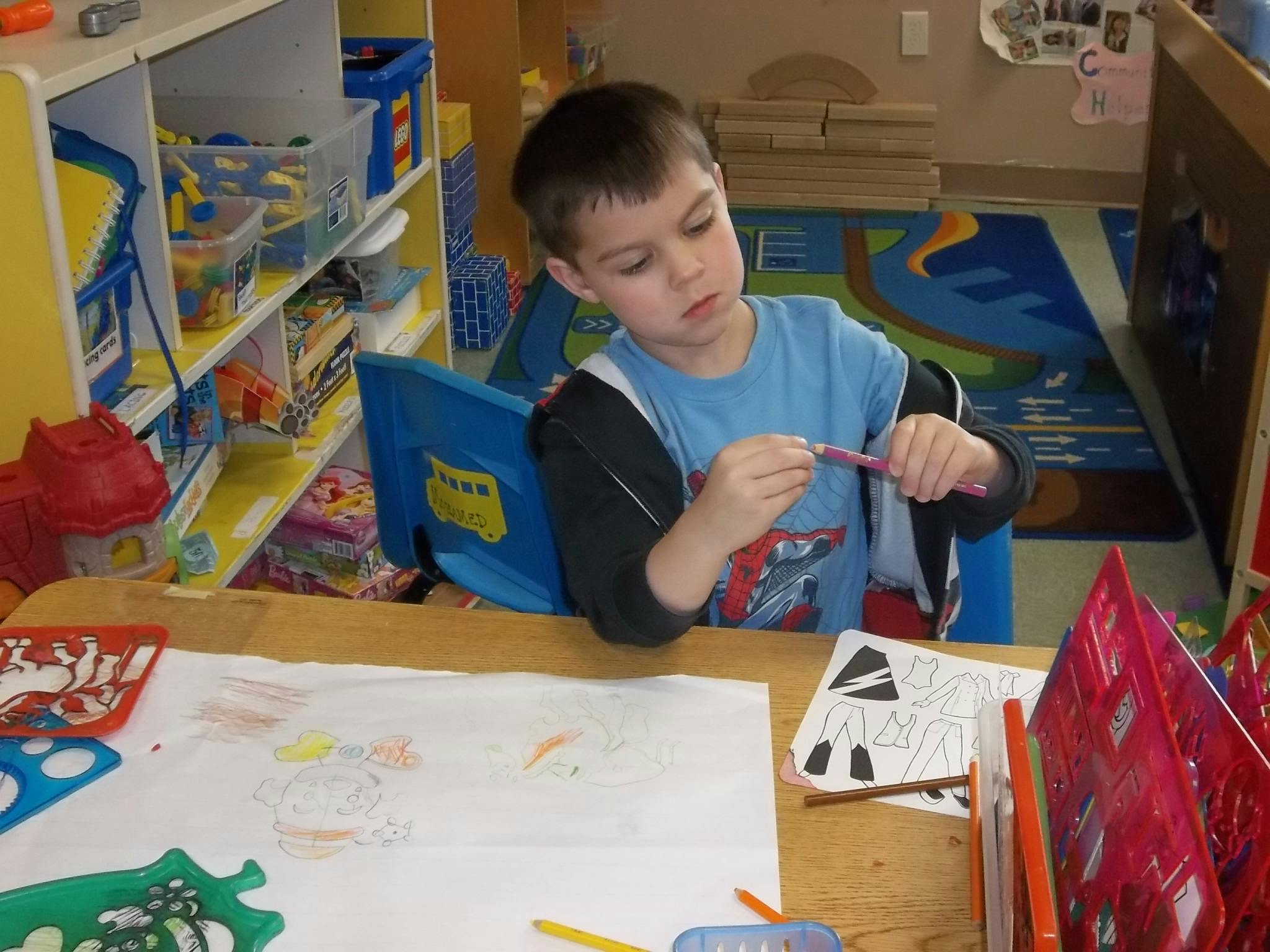 Child sitting at a table holding a crayon in a classroom