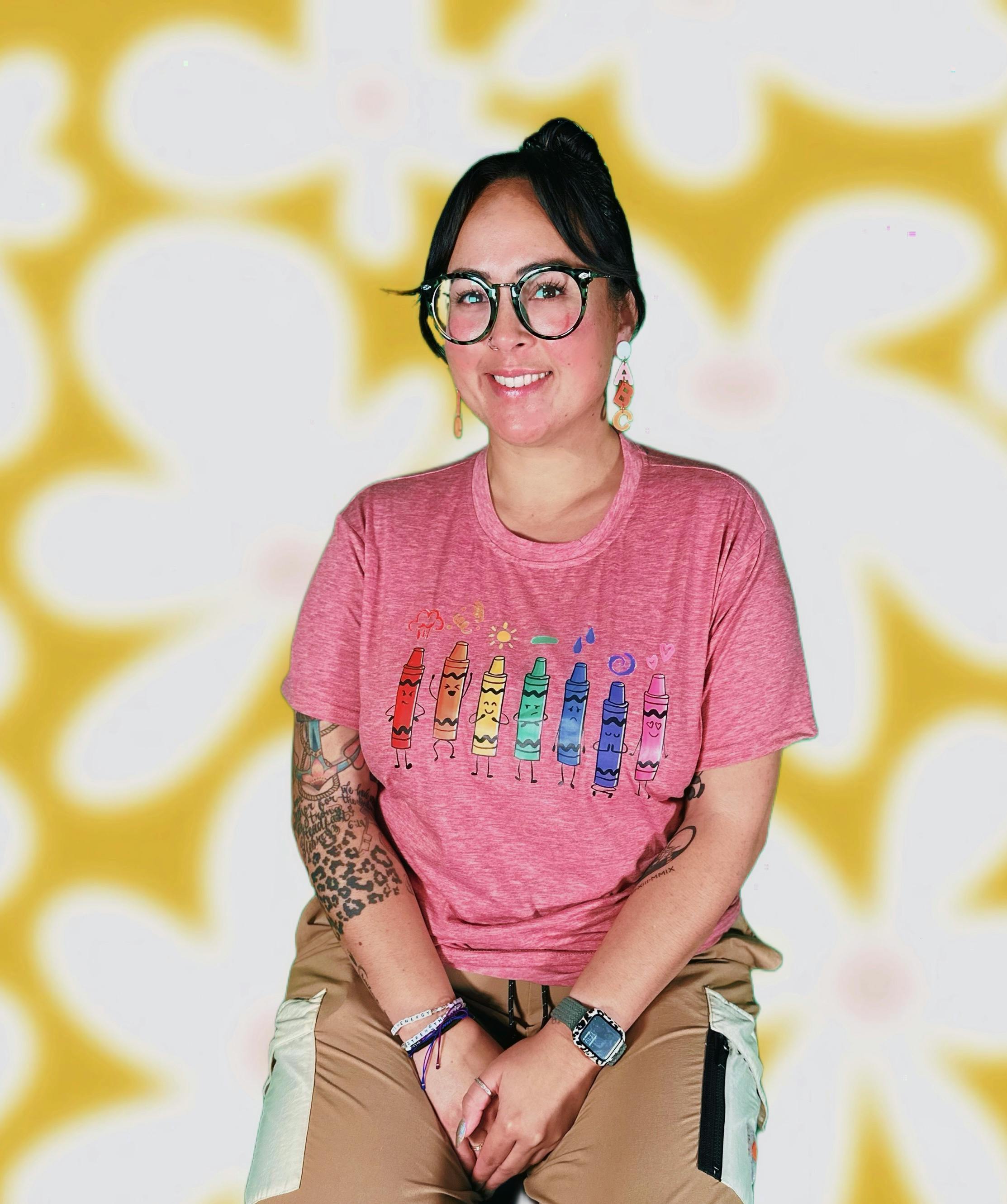 Person wearing glasses and a pink shirt with crayon drawings