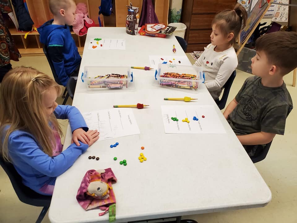 Children at a table with papers and small colorful objects