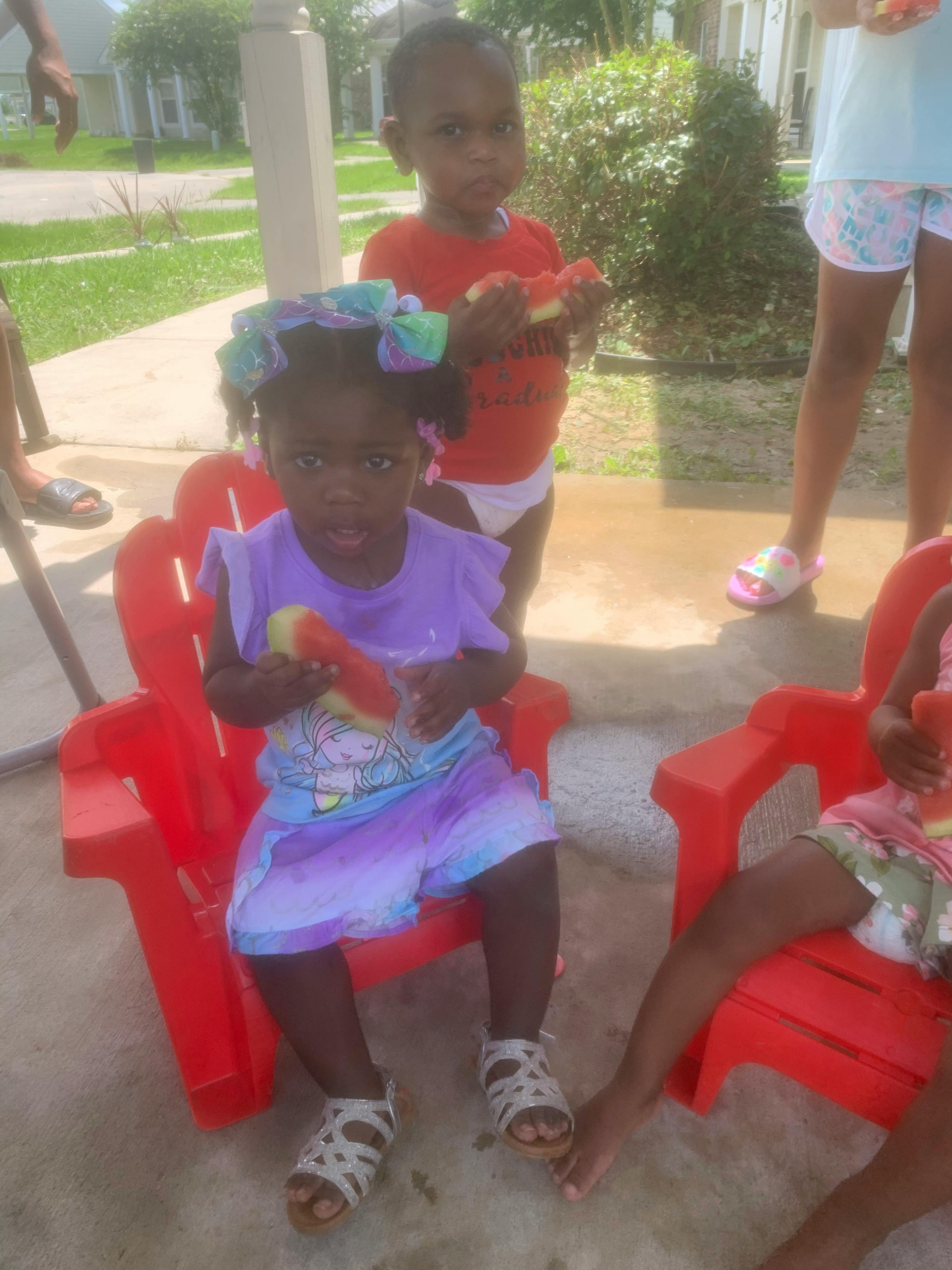 Child sitting in a red chair holding a piece of watermelon