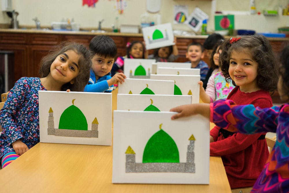 Children in a classroom holding up drawings of a green dome building with gold dome building