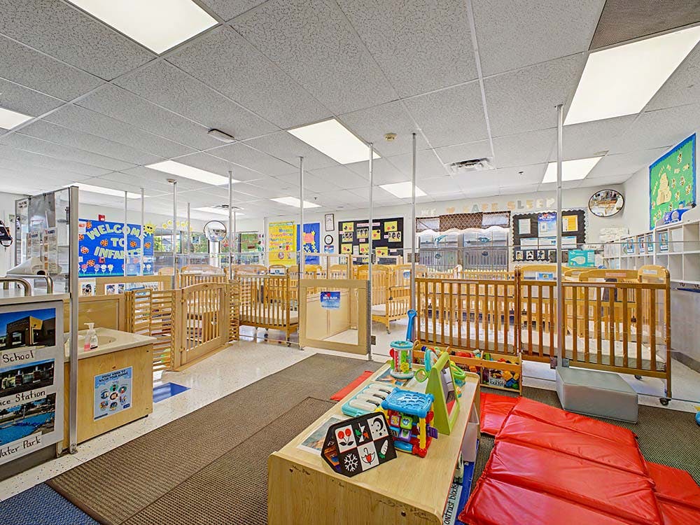 An empty infant care classroom with multiple cribs and play areas