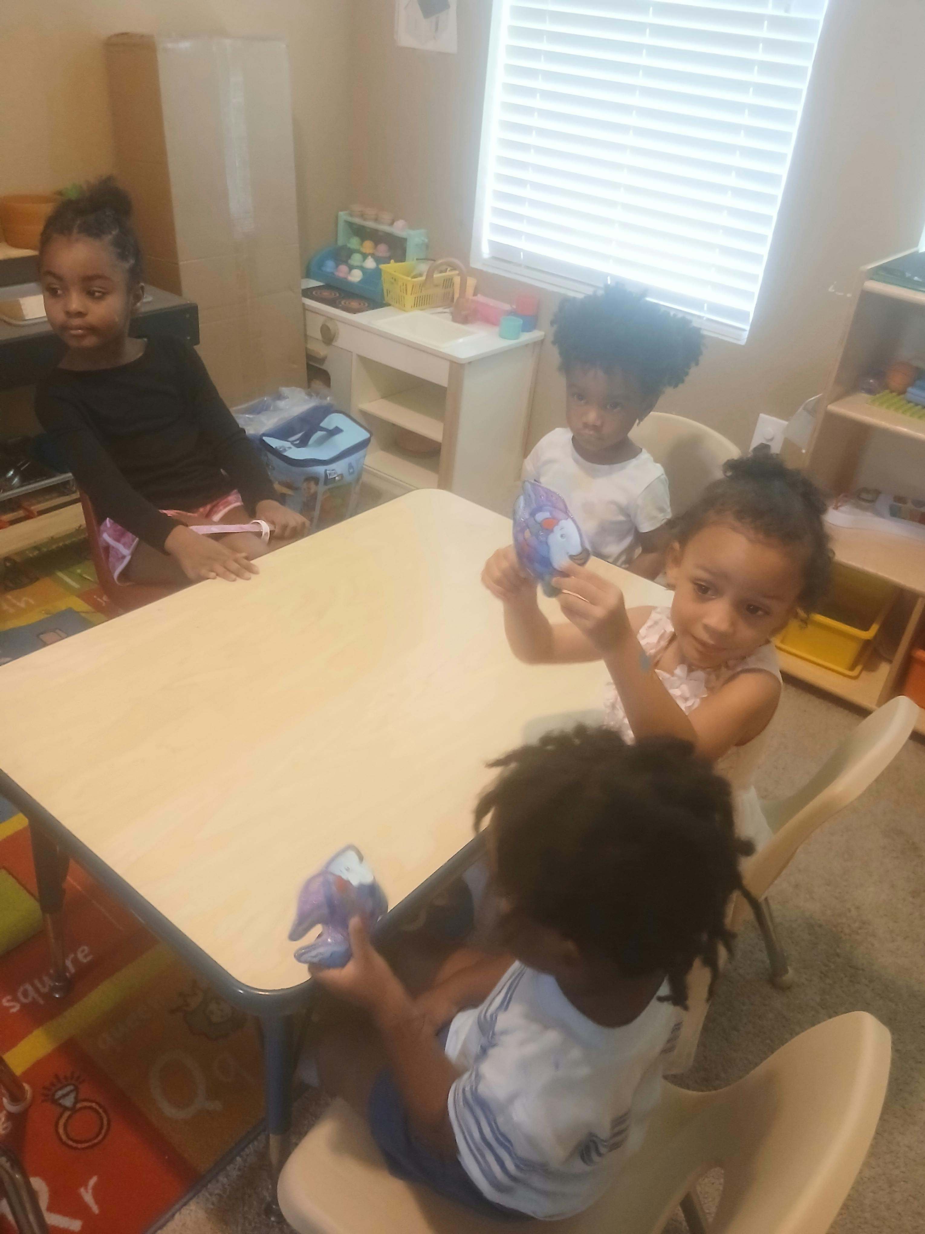 Four children sitting around a table, two holding small toys