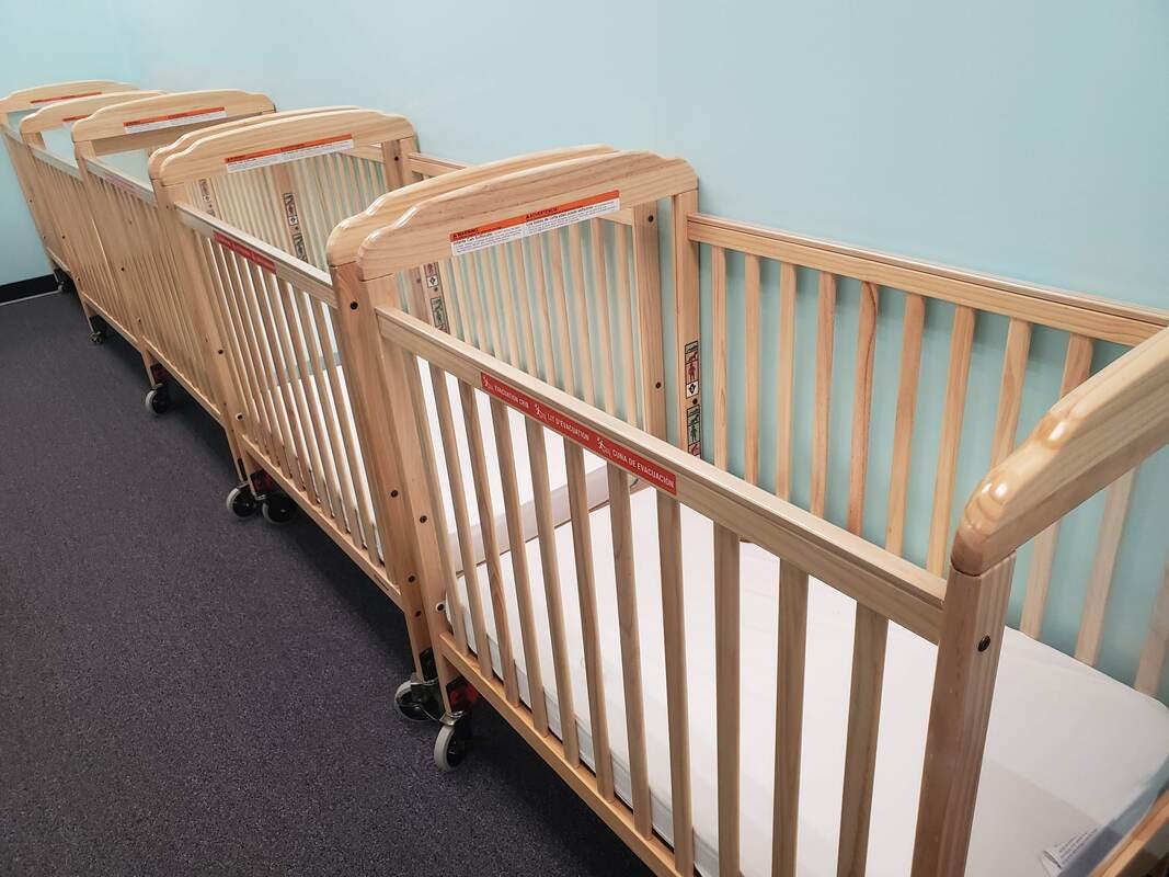 Row of empty wooden cribs with mattresses
