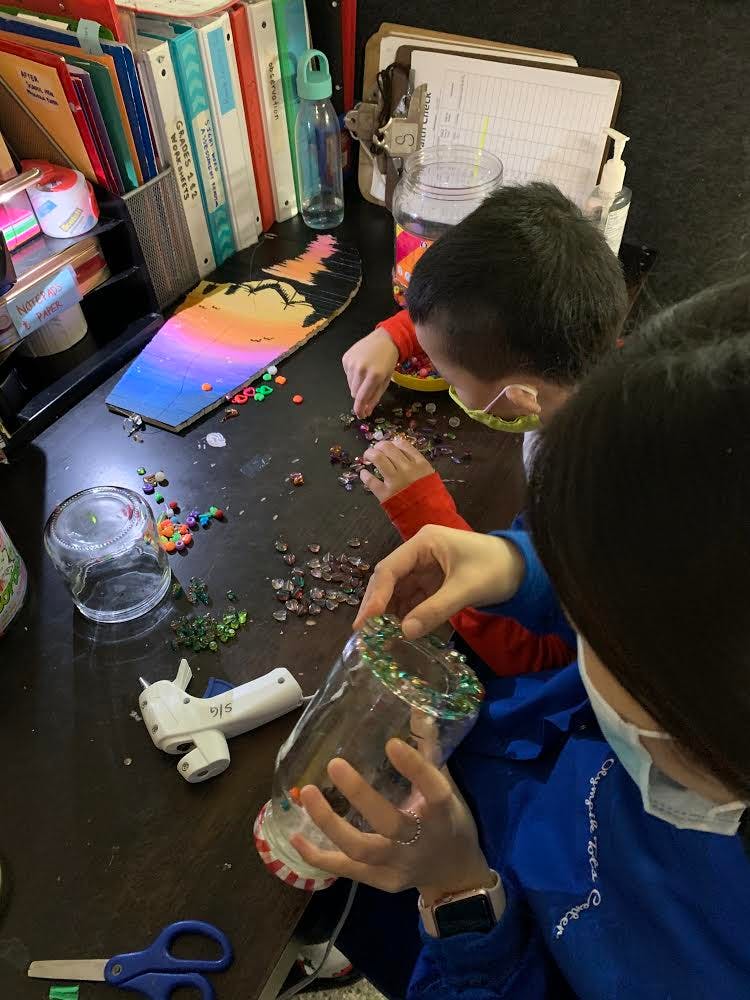 Two people decorating jars with small beads and a glue gun