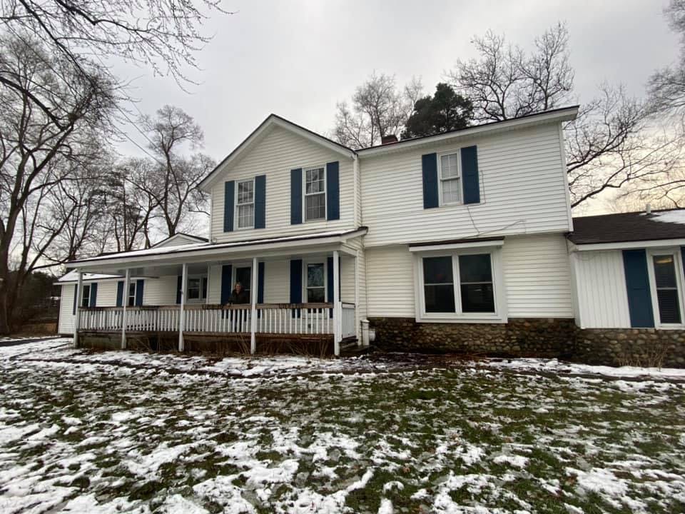 White house with dark shutters and a porch, snow on the ground