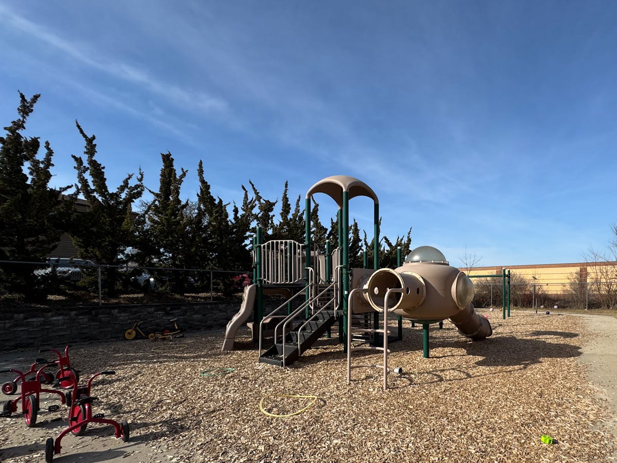 A playground with a climbing structure, slides, and tricycles on wood chips