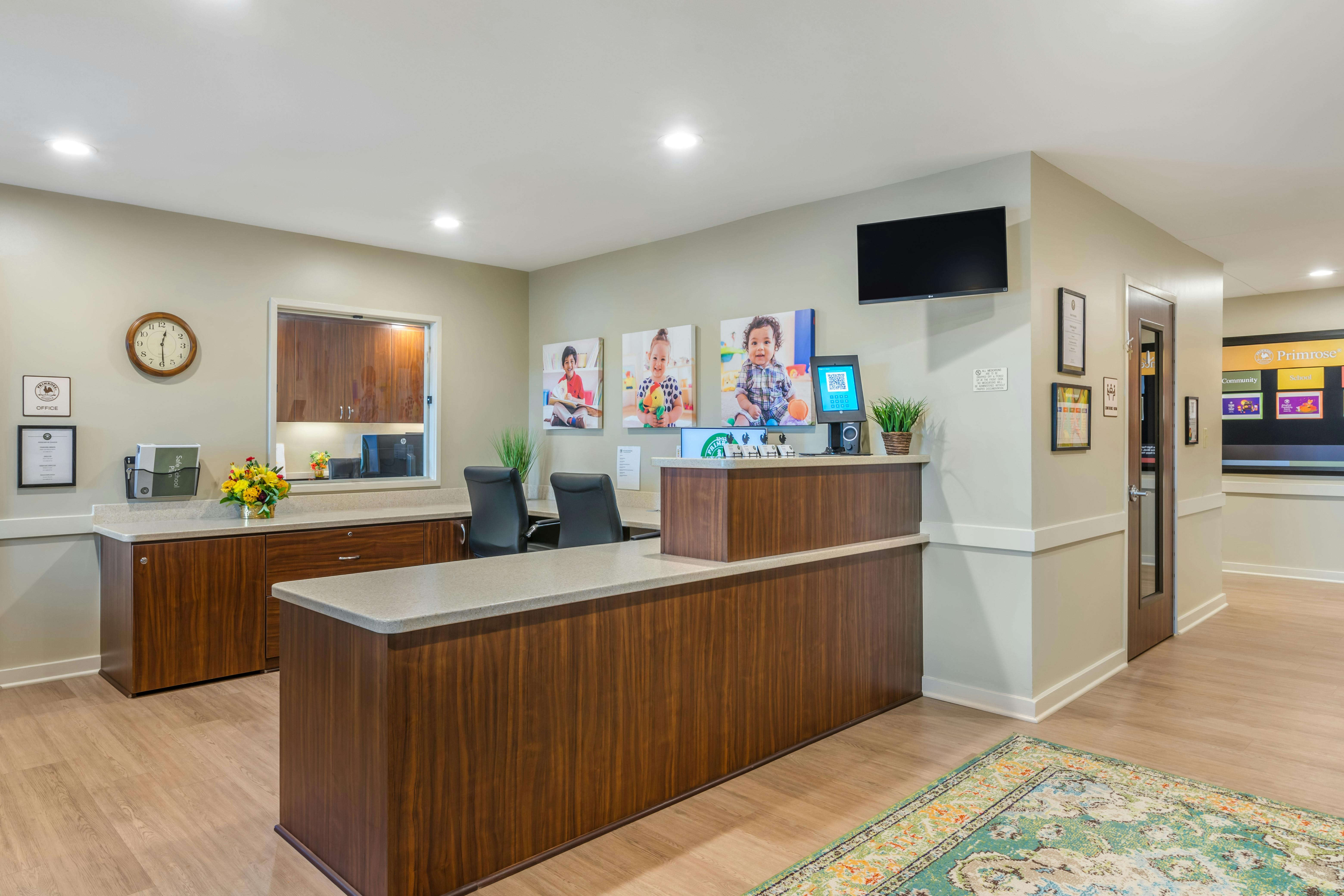 Reception desk in an office with pictures of children, a clock, and a monitor