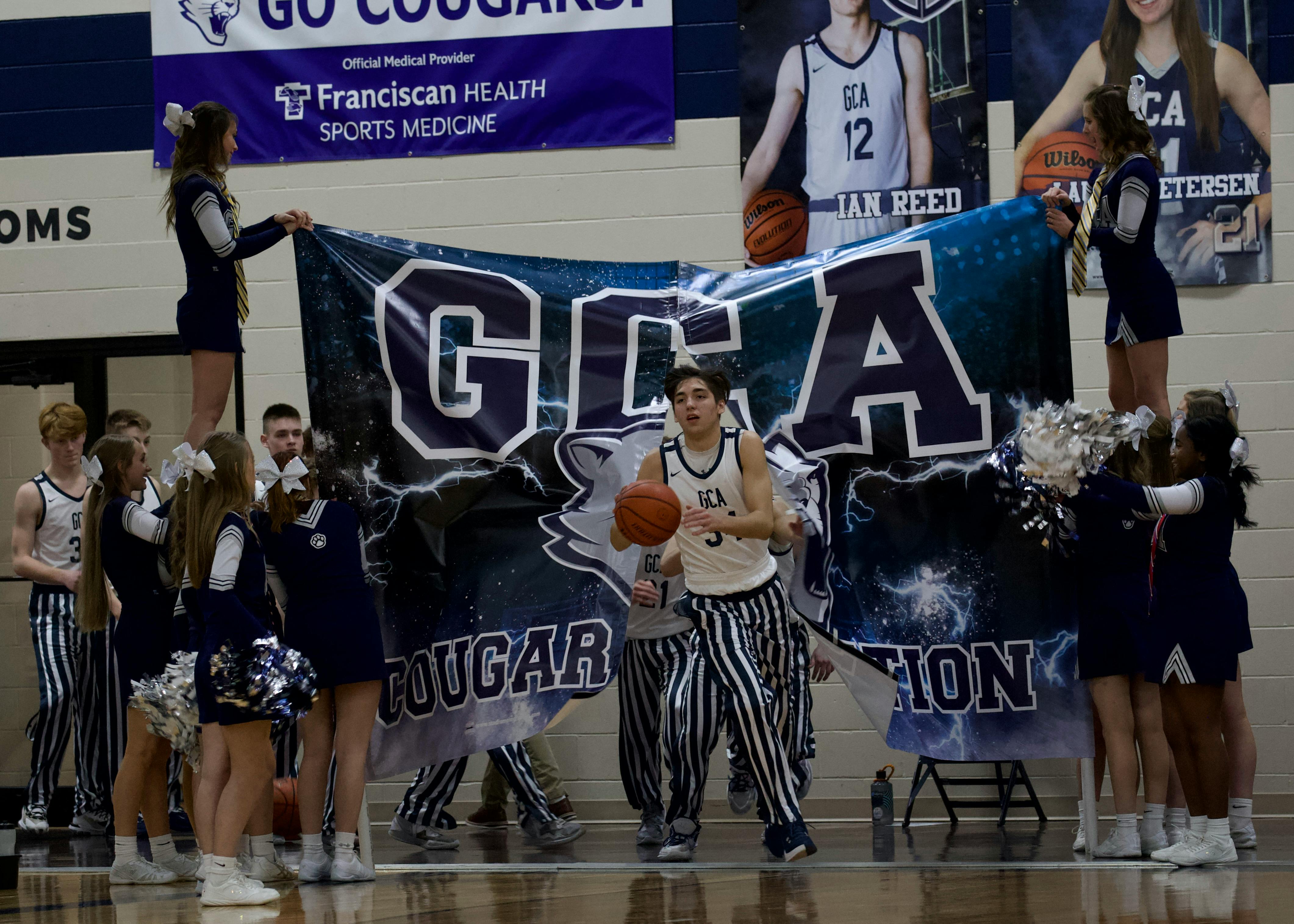 Person in striped pants holding a basketball with cheerleaders and banner