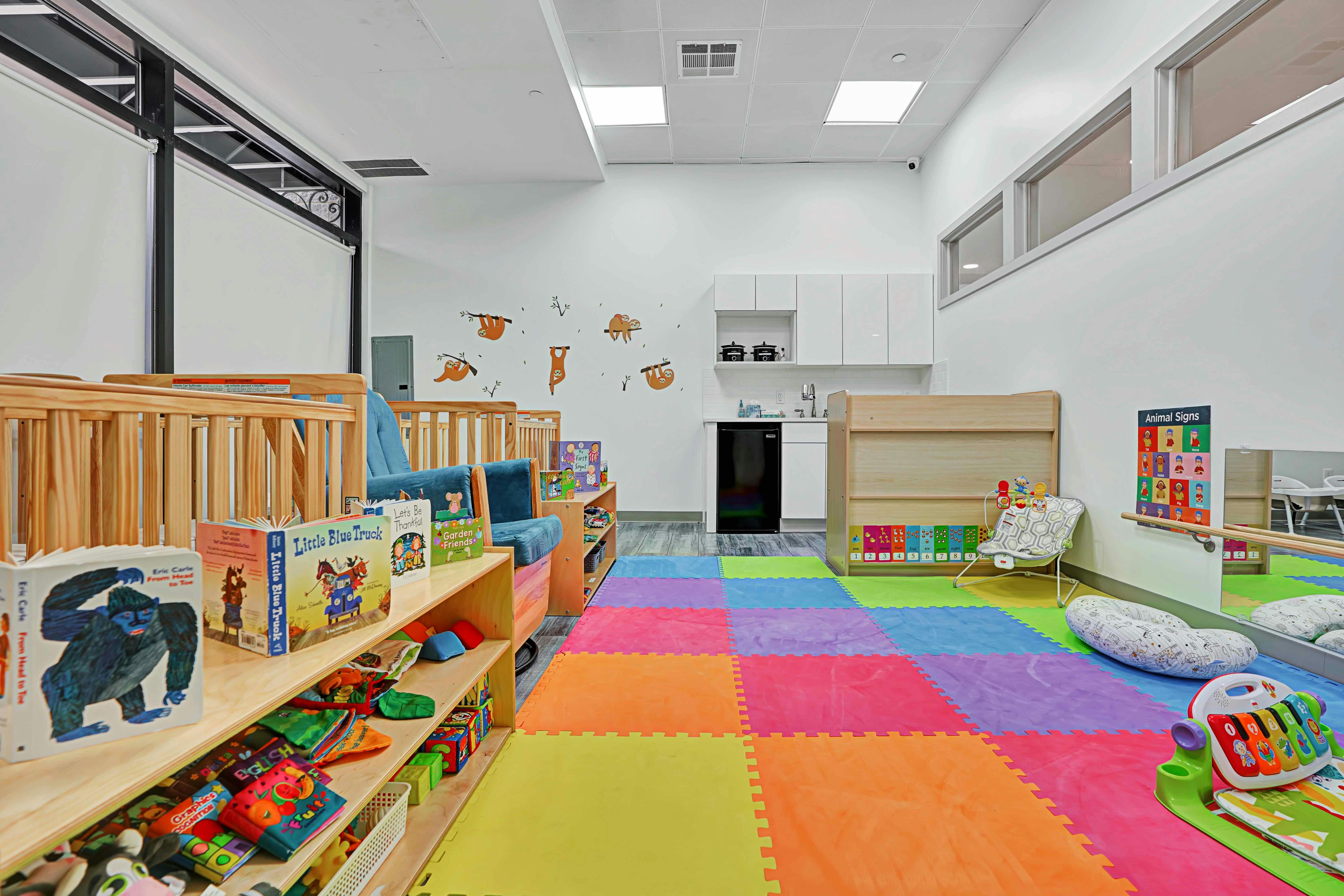 Playroom with colorful floor mats, cribs, and shelves of books and shelves of toys