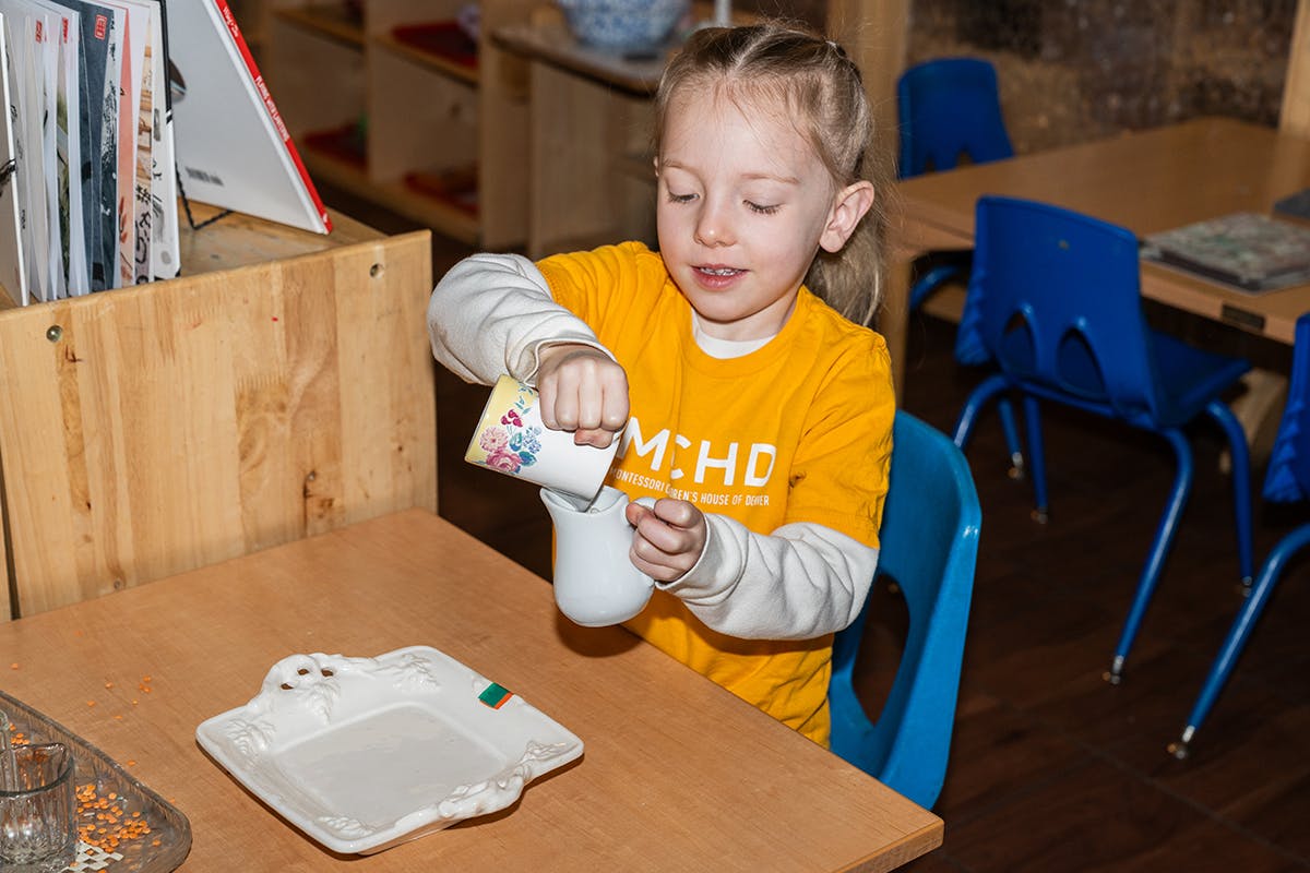 Child pouring from a small container into a cup at a table