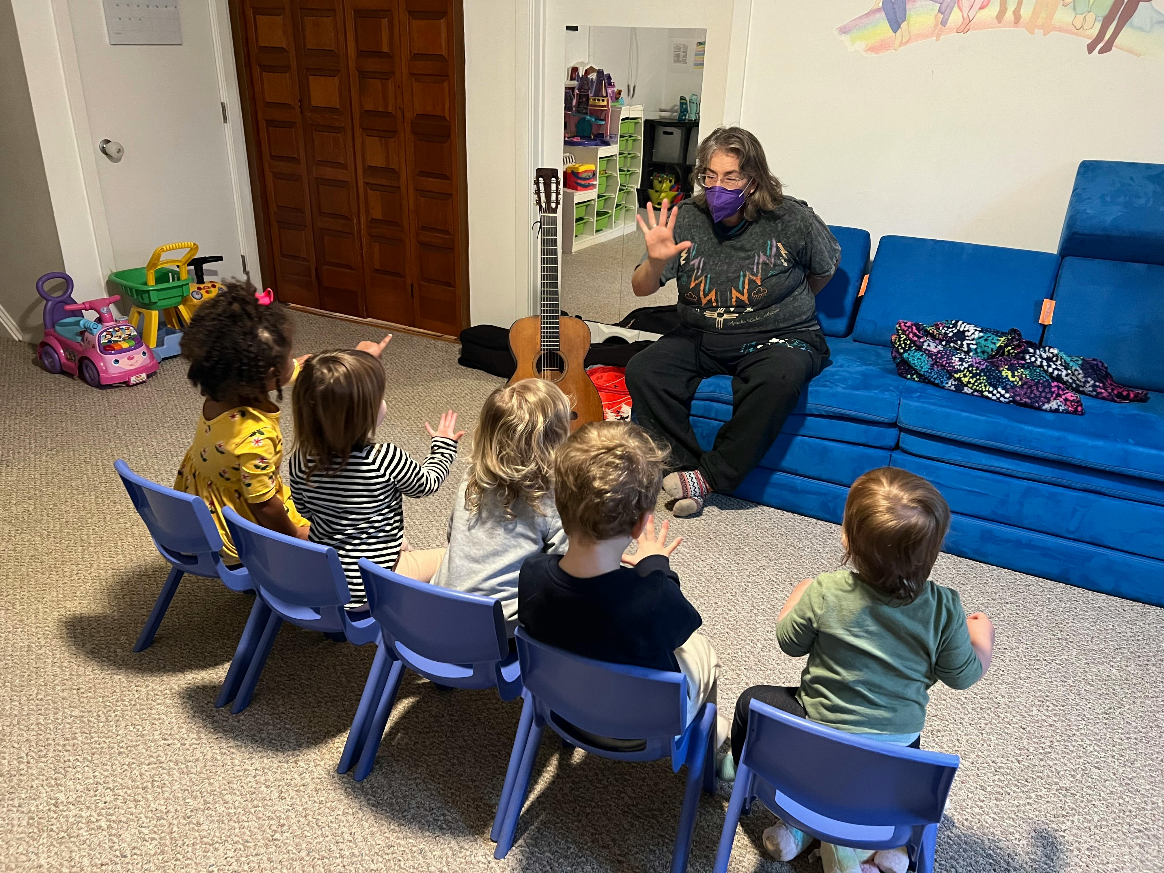 Person wearing a mask interacting with children seated in chairs