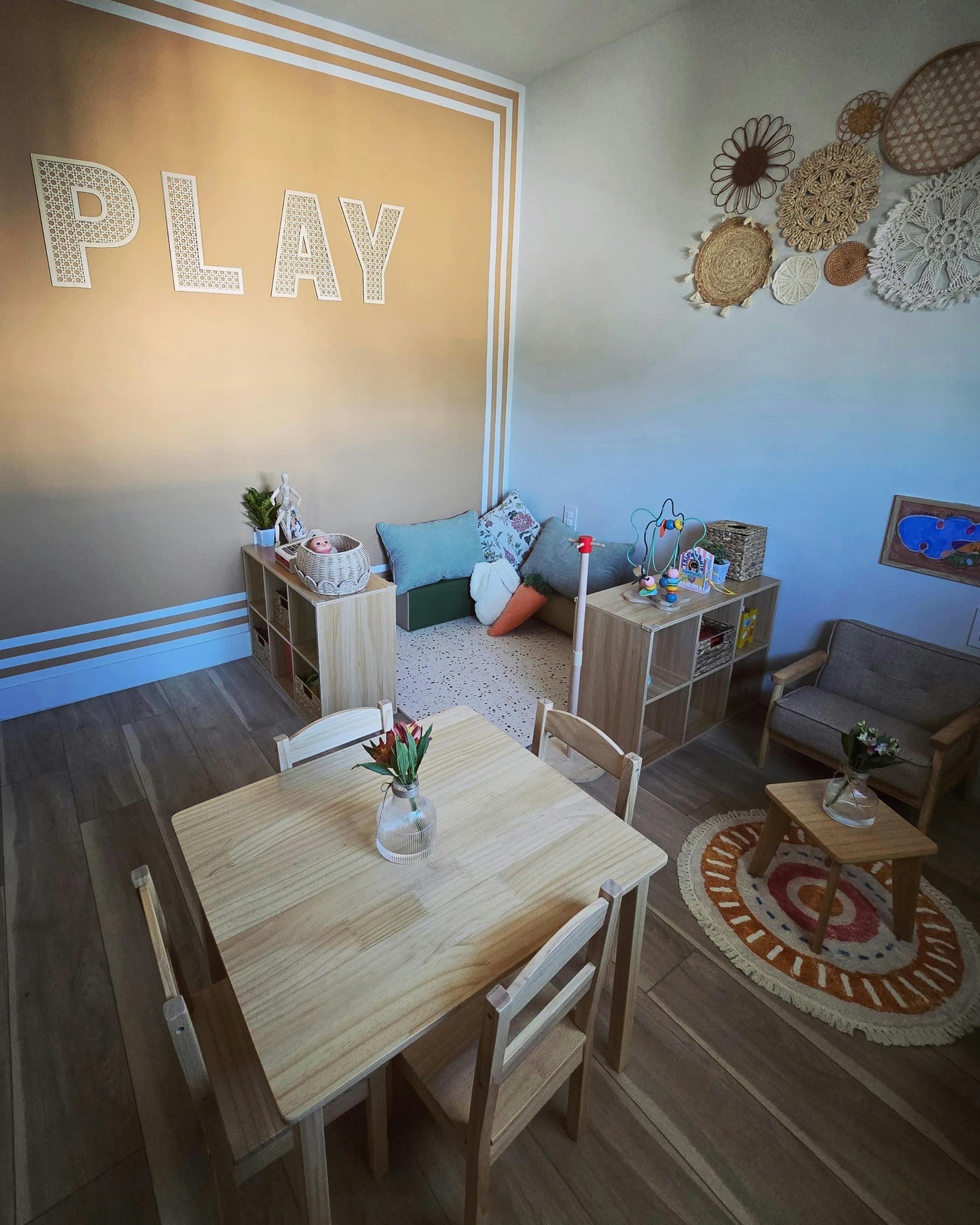 Room with a small table and chairs, cushions, and the word PLAY on the wall